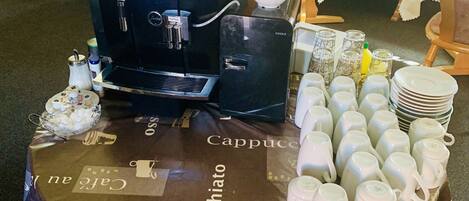 A coffee station with a coffee machine, cups, and a table covered with a branded tablecloth.