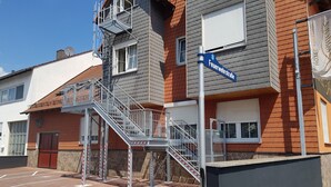 A building with a metal staircase leading to a balcony, a sign reading "Feuerwehrstraße," and a gated entrance.