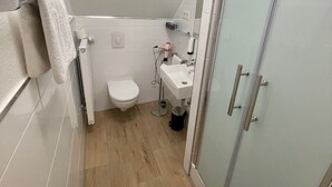 A small, modern bathroom with a toilet, sink, and glass shower enclosure.