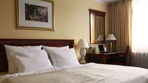 A hotel room with a large bed, two bedside lamps, a desk with a laptop, and a framed picture on the wall.