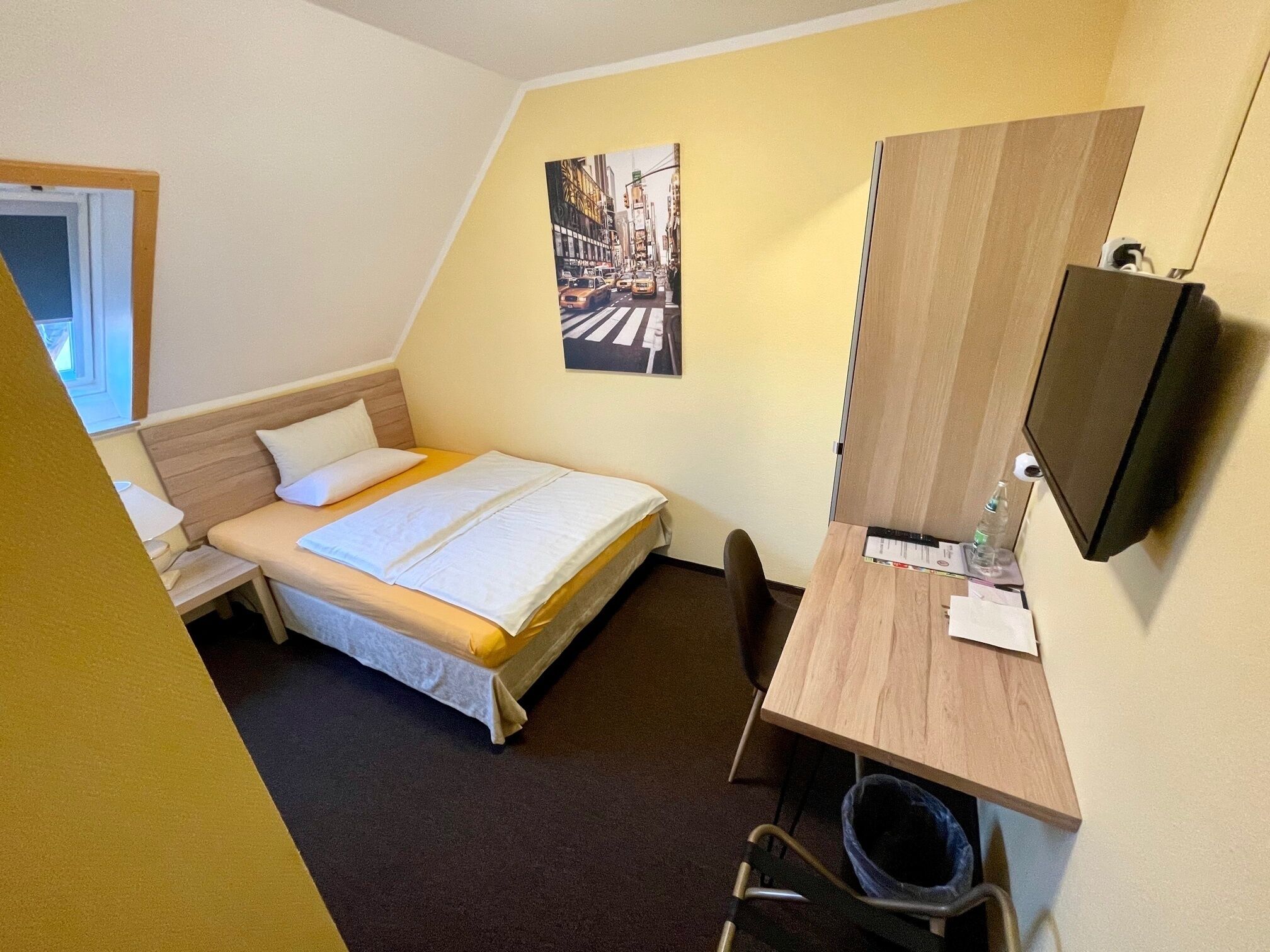 Ein Hotelzimmer mit Bett, Schreibtisch, Stuhl, Fernseher und einem Bild an der Wand.