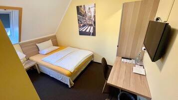 Ein Hotelzimmer mit Bett, Schreibtisch, Stuhl, Fernseher und einem Bild an der Wand.