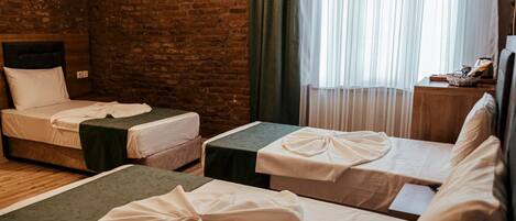 A hotel room with two single beds, a brick wall, a wooden headboard, a window with sheer curtains, and a nightstand with a lamp.
