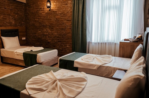 A hotel room with two single beds, a brick wall, a wooden headboard, a window with sheer curtains, and a nightstand with a lamp. - HASUNİ TAŞ HOTEL (Diyarbakir)