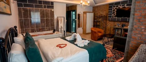 Habitación de hotel con una cama grande, chimenea, zona de estar y vistas al exterior.