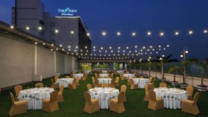 An outdoor banquet hall with multiple round tables, each set with white tablecloths and brown chairs, under string lights. - The Fern Residency Navi Mumbai, Turbhe, Series by Marriott (Navi Mumbai)