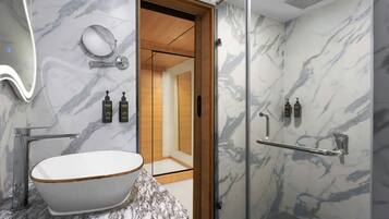 A modern bathroom with a freestanding bathtub, a glass shower enclosure, and marble walls.