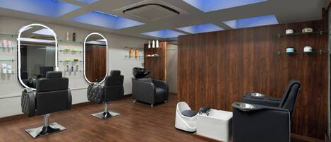 A modern salon with wooden flooring, multiple seating areas, and built-in mirrors.