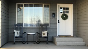 Un portico con due poltrone a dondolo, un tavolino e una porta bianca decorata con una ghirlanda.
