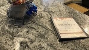 Cucina con piani di lavoro in granito, mobili bianchi, una macchina da caffè e un libro degli ospiti sul bancone.