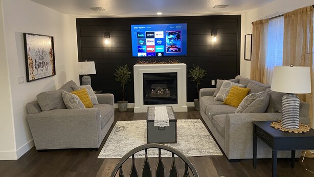 Un soggiorno moderno con due divani grigi, un tavolino da caffè nero, un caminetto e una televisione a schermo piatto posizionata sopra il camino.