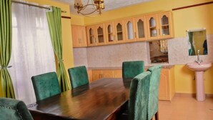 Une salle à manger avec une table en bois et des chaises recouvertes d’un tissu vert, une cuisine avec des meubles en bois et un évier.