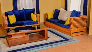 Une pièce comprenant deux canapés : l’un a une structure en bois et des coussins bleus, l’autre a également une structure en bois, mais avec des coussins jaunes. Une table basse en bois se trouve devant les canapés.