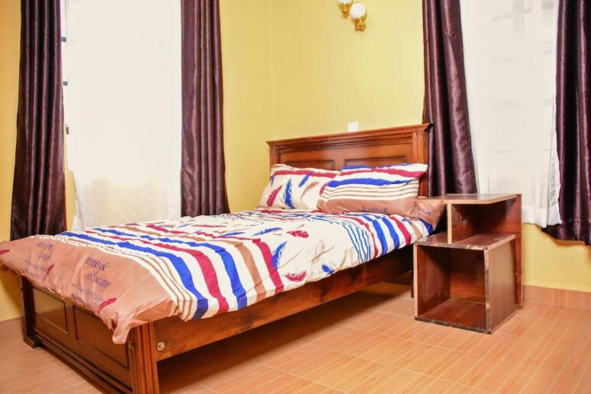 A single bed with a striped blanket, a wooden headboard, and a nightstand with a square wooden base.