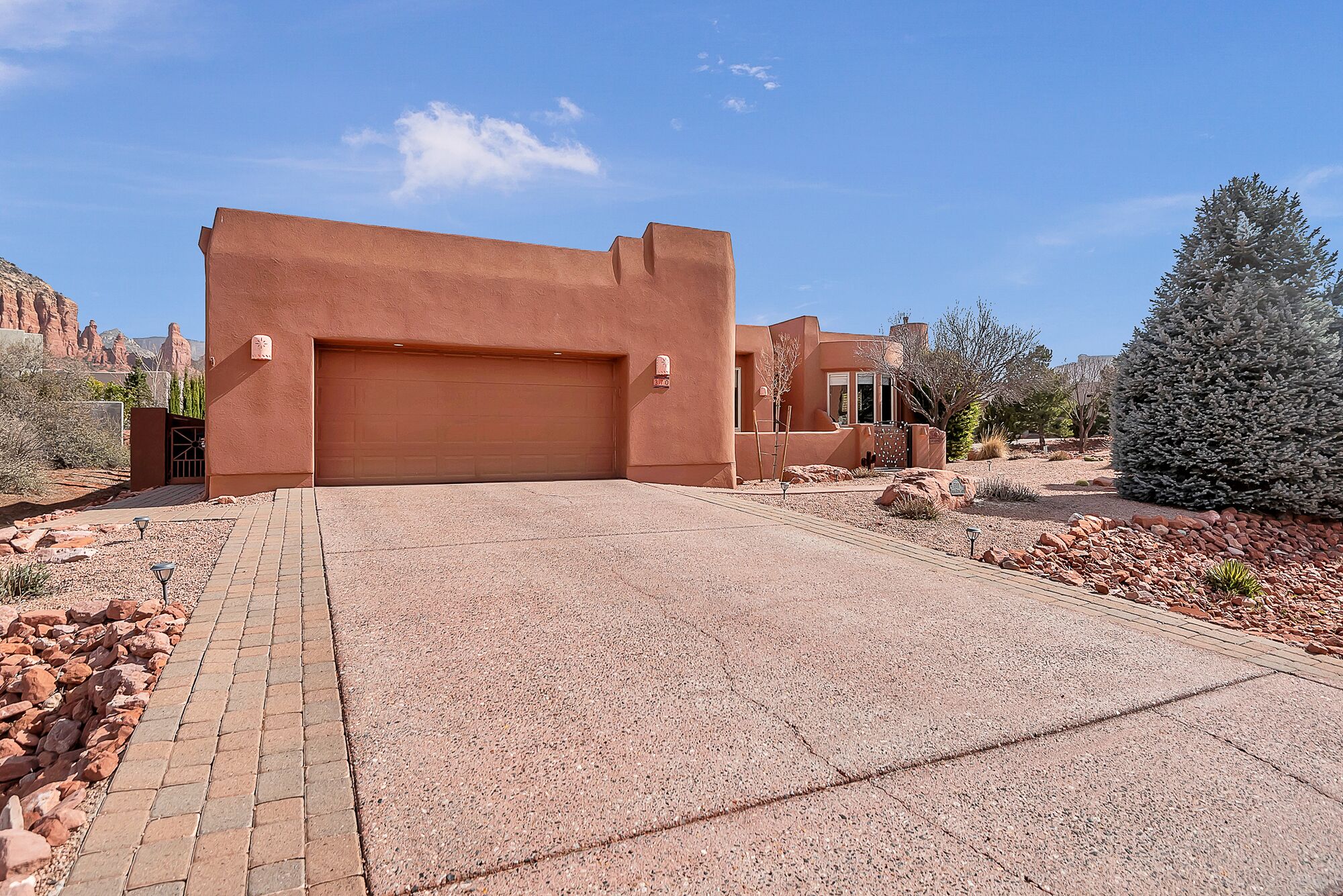 A desert-style house with a large garage, paved driveway, and surrounding rocky terrain.