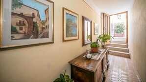 Un pasillo con obras de arte enmarcadas, una consola de madera, plantas en macetas y vistas a una escalera que lleva a un balcón.