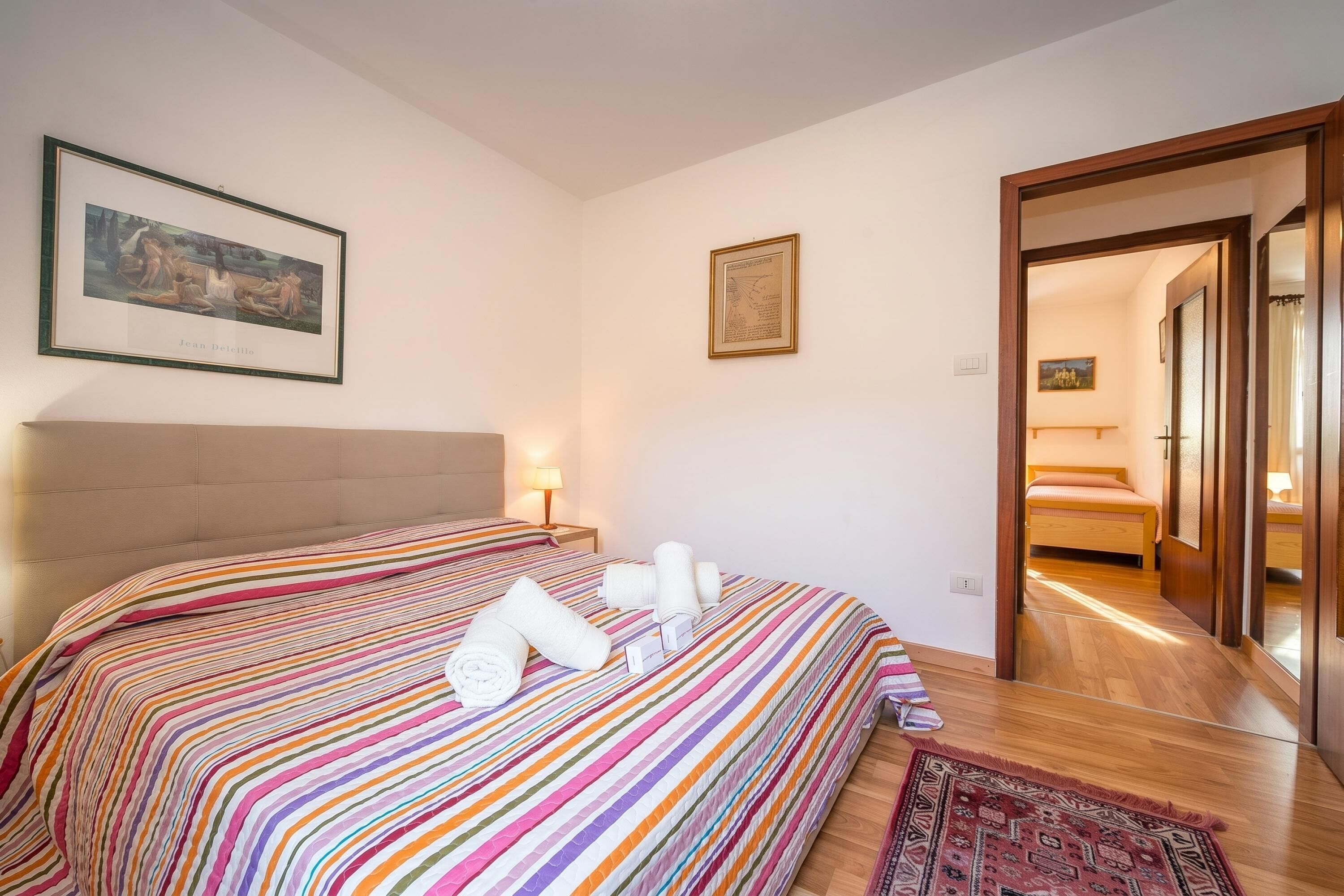A hotel room with a striped bedspread, a framed painting, and a wooden floor.