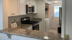 A kitchen with white cabinets, a microwave, a stove, and granite countertops. - Surf Court Unit #1-Remodeled villa across the street from the ocean (Hilton Head Island)