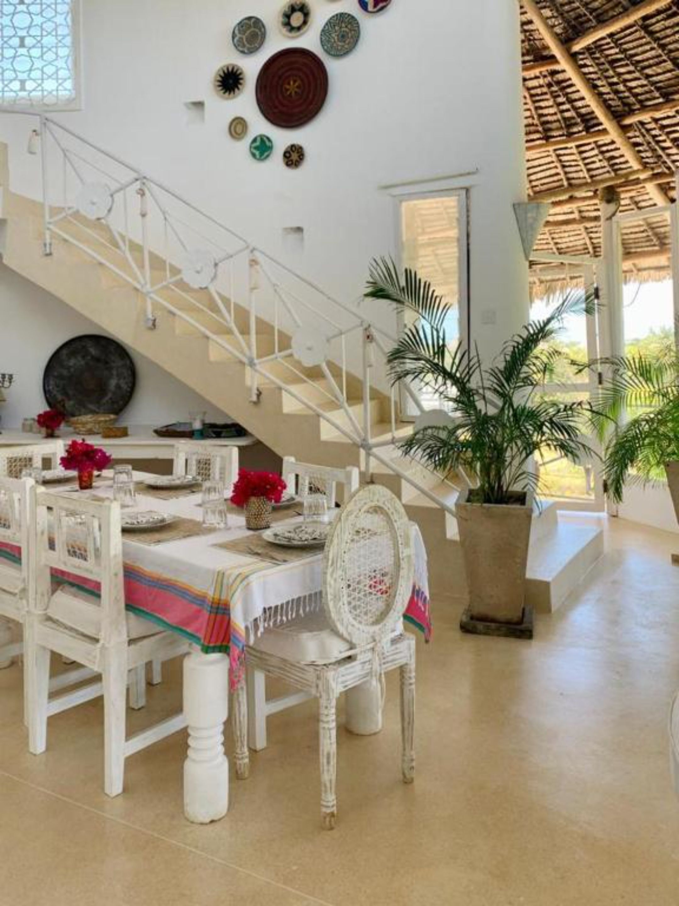 A dining area with white furniture, a staircase, and decorative plates on the wall.