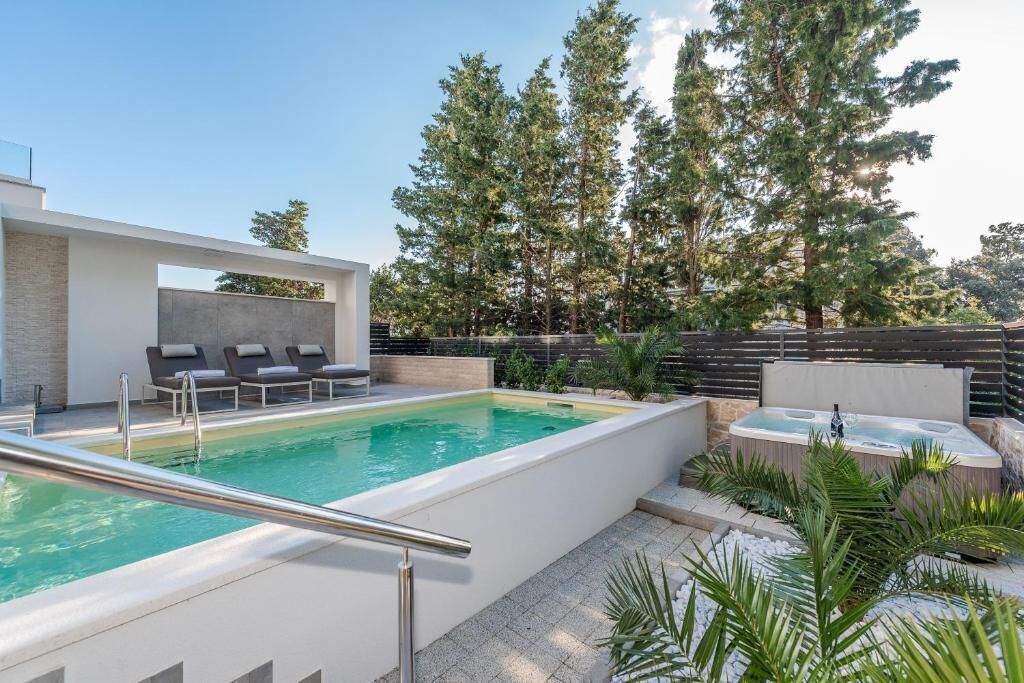 A modern outdoor pool area with a hot tub, lounge chairs, and a stone wall.
