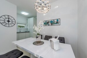 A modern dining area with a white table, black chairs, a decorative vase with white flowers, a clock, and a unique chandelier. - Sunset apartment with private pool and jacuzzi  (Novalja)
