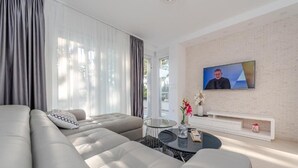 Ein modernes Wohnzimmer mit einem großen grauen Sofa, einem runden Couchtisch und einem Flachbildfernseher, der an einer Ziegelwand angebracht ist.