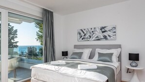 Ein modernes Schlafzimmer mit einem großen Bett, Meerblick und minimalistischer Einrichtung.