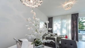Ein modernes Wohnzimmer mit einer weißen Orchidee als Blickfang, einem Kronleuchter und Blick ins Freie durch große Fenster.