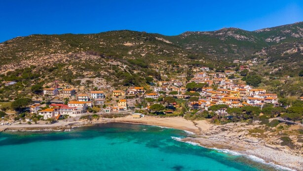 Un pueblo costero con edificios en una ladera que domina una playa turquesa.