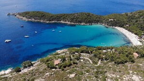 Eine Küstenlandschaft mit klarem, blauem Meer, einem Sandstrand und hügeligem Gelände mit verstreuten Gebäuden.