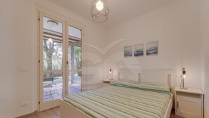 Ein Schlafzimmer mit Bett, Nachttisch, Lampe, Fenster und Tür.