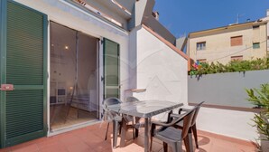 Eine Terrasse mit Tisch und Stühlen, eine Schiebetür und eine weiße Wand mit einer Hauskontur.