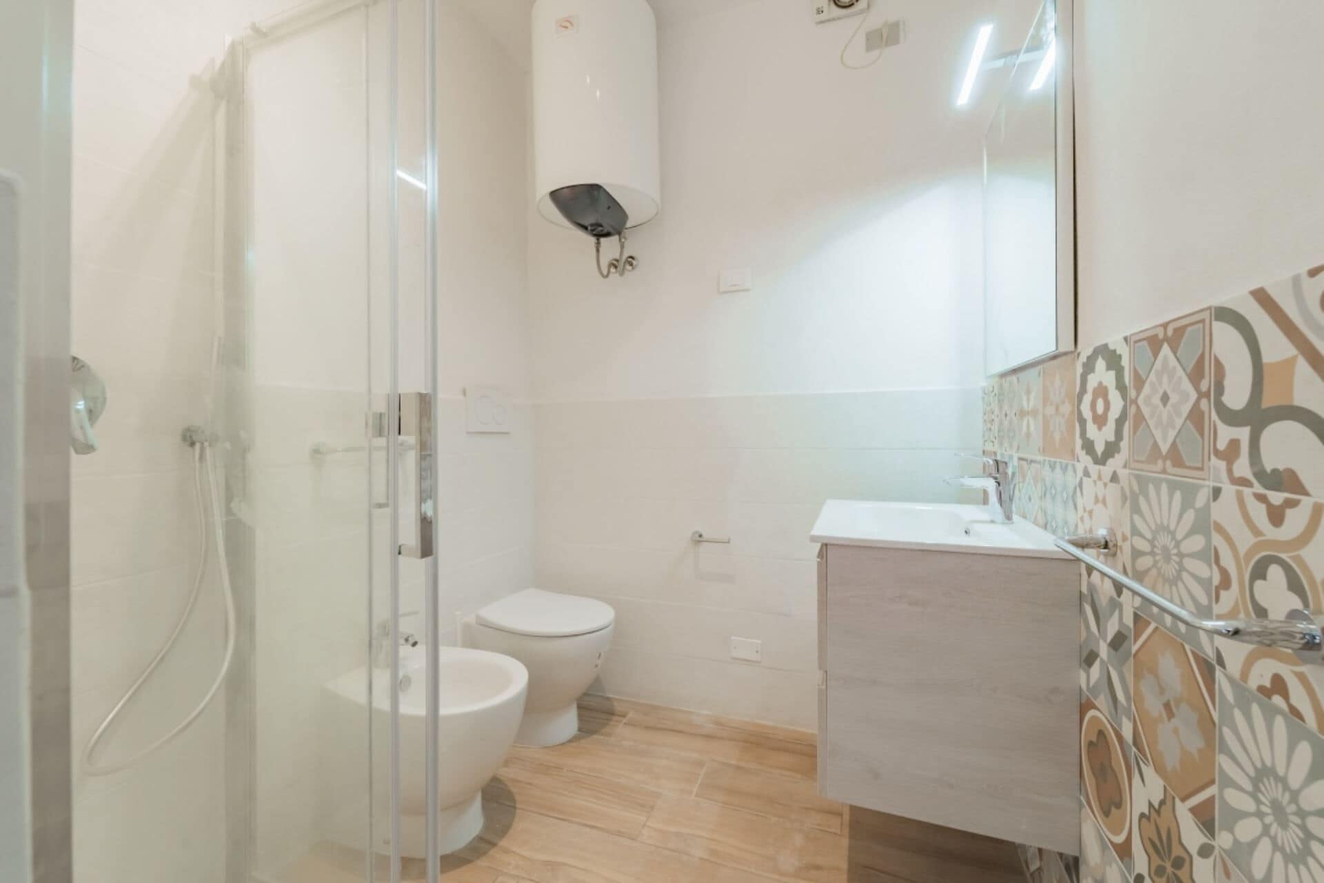 Un bagno con cabina doccia in vetro, un water e un lavabo con pannelli decorativi in ceramica.