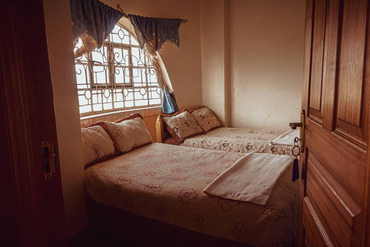 Ein Schlafzimmer mit zwei Betten, einem Fenster mit Gitterstäben und einem hölzernen Kleiderschrank.