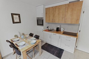 Una cocina compacta con armarios blancos, encimera de madera y zona de comedor con una mesa dispuesta para cuatro comensales.