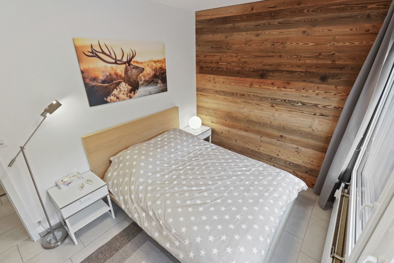 Een slaapkamer met een houten wandpaneel, een bed met een sterrenbedekking, een nachtkastje met een lamp en een schilderij van een hert aan de muur.
