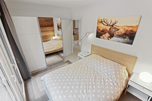 Un dormitorio moderno con una cama, una mesita de noche, un escritorio, un espejo y un cuadro de un ciervo colgado en la pared.