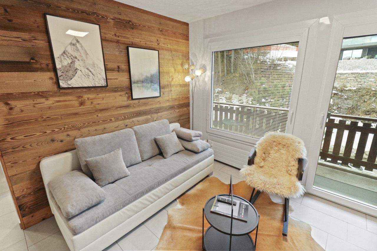 Un salon moderne avec un canapé gris, un lambris en bois, une grande fenêtre avec des stores et un fauteuil en fourrure.