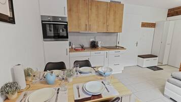 Una cocina moderna con armarios de madera, horno empotrado y un comedor preparado para cuatro personas, con mesa, sillas y sofá.
