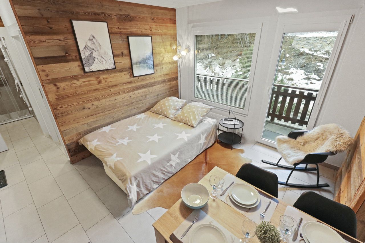 Une pièce comprenant un lit, une table à manger dressée avec des assiettes et des verres, une chaise, et donnant sur l’extérieur.
