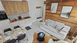 Una cocina moderna con armarios de madera, un comedor con una mesa lista para cuatro personas y una sala de estar con un sofá y una alfombra mullida.