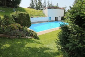 Una piscina rodeada de exuberante vegetación y un pequeño edificio con techo rojo.