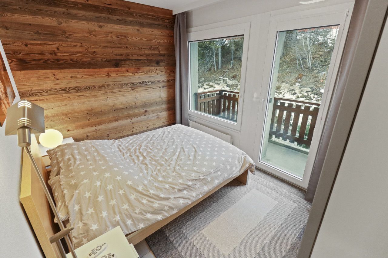 Un dormitorio con cabecera de madera, cama con colcha estampada de estrellas, lámpara de noche y vistas a una terraza de madera a través de una puerta corrediza de vidrio.