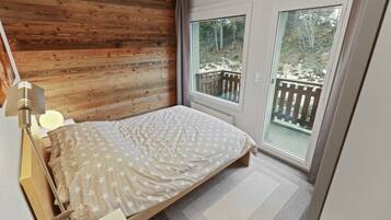 Un dormitorio con cabecera de madera, cama con colcha estampada de estrellas, lámpara de noche y vistas a una terraza de madera a través de una puerta corrediza de vidrio.