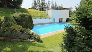 A swimming pool surrounded by lush greenery and a small building with a red roof.