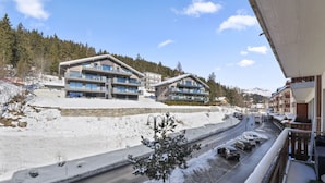 A modern hotel with multiple floors, a ski slope in the background, and a road with parked cars.