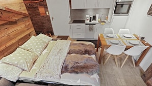 A compact room with a bed, a dining table set for four, and a kitchenette.