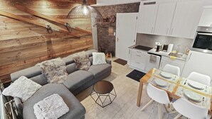 A modern kitchen with white cabinets, a dining table set for four, and a gray sofa with fluffy cushions.
