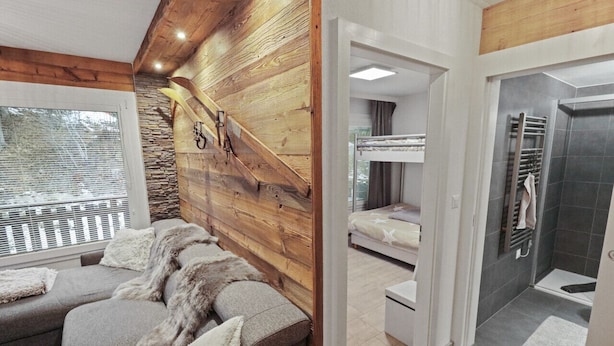 A modern interior with a wooden accent wall, a sofa with fur throw pillows, a bunk bed, and a shower area.