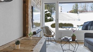 A cozy room with a wooden floor, a rocking chair, a small table with a plant, and a sofa. - Studio rénové et élégant en plein centre (Crans-Montana)